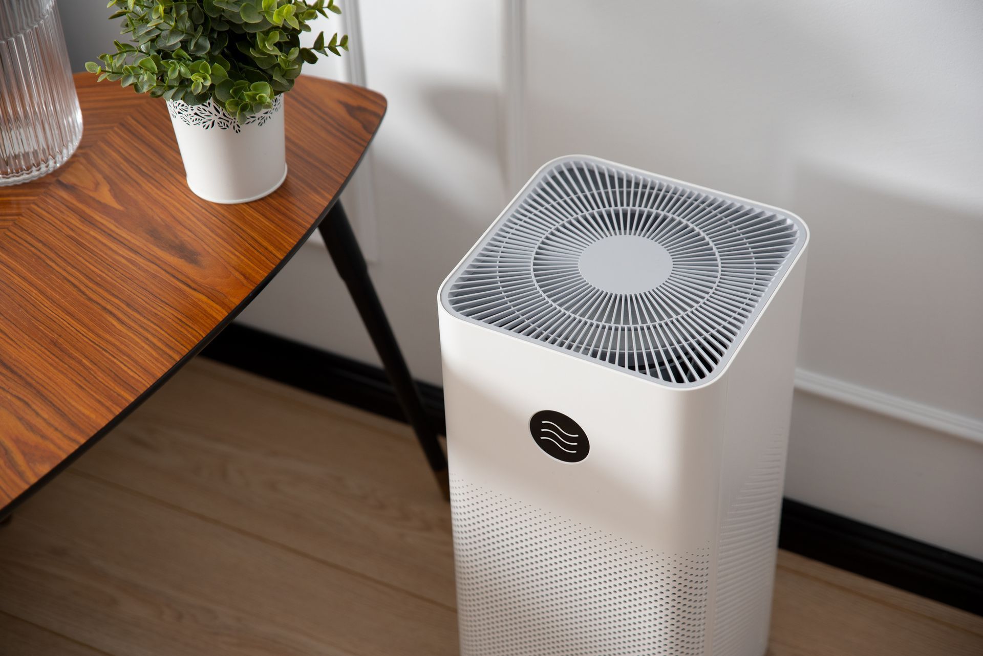 A white air purifier is sitting on the floor next to a wooden table.