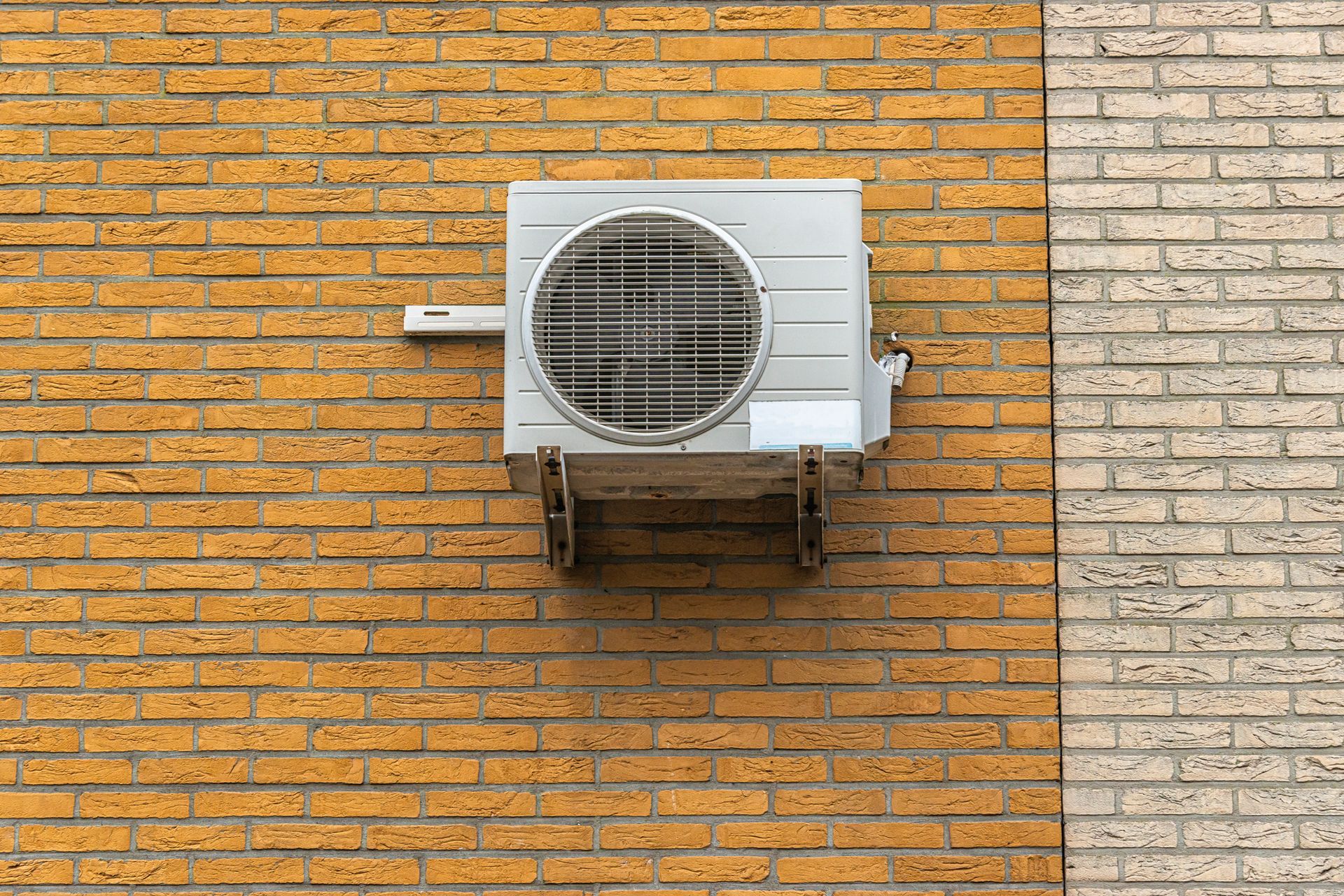 A white air conditioner is mounted on a brick wall.