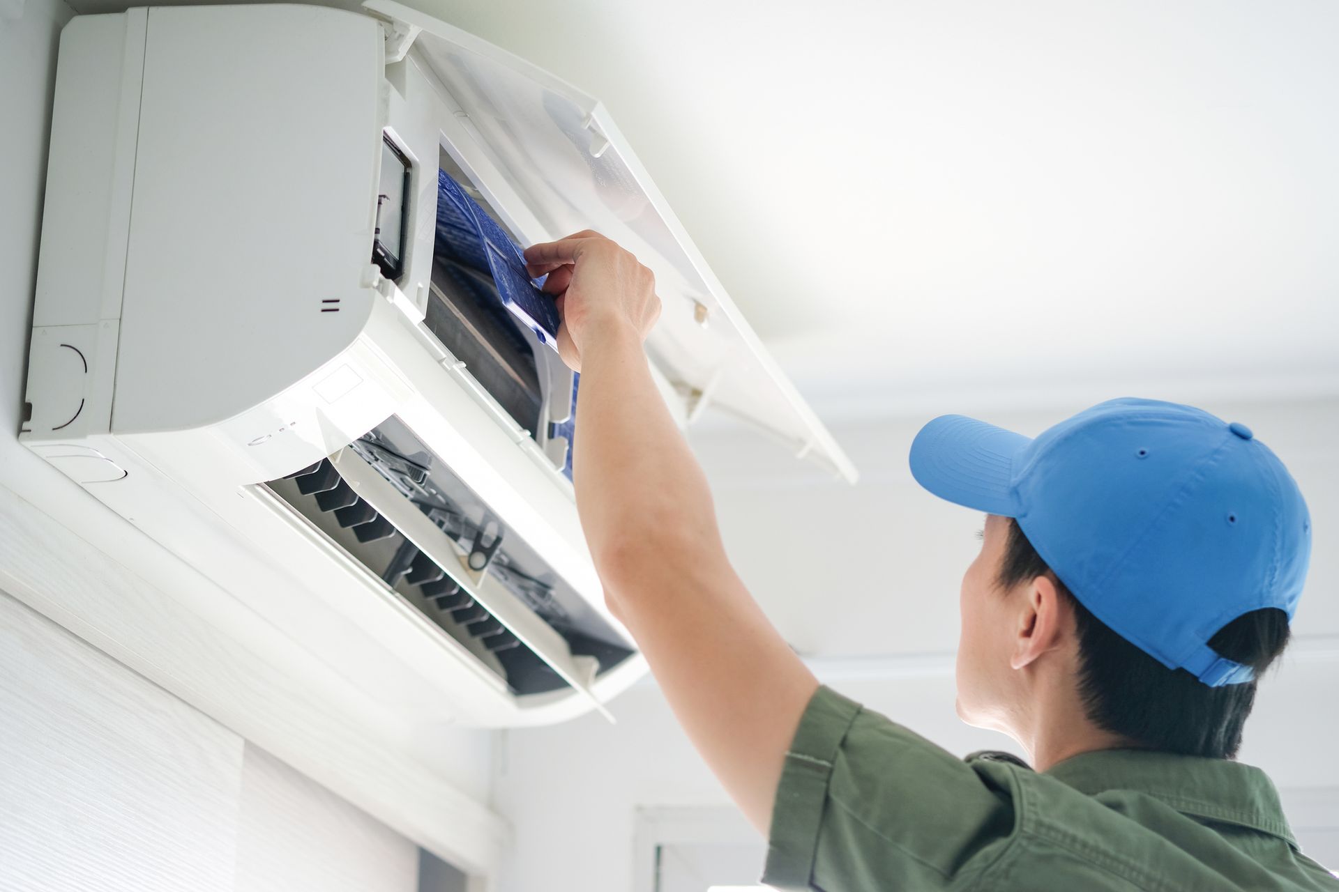 A man in a blue hat is cleaning an air conditioner.