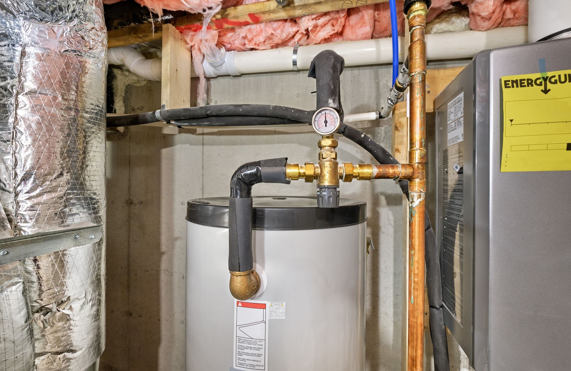 A water heater is sitting in a basement next to a heater.