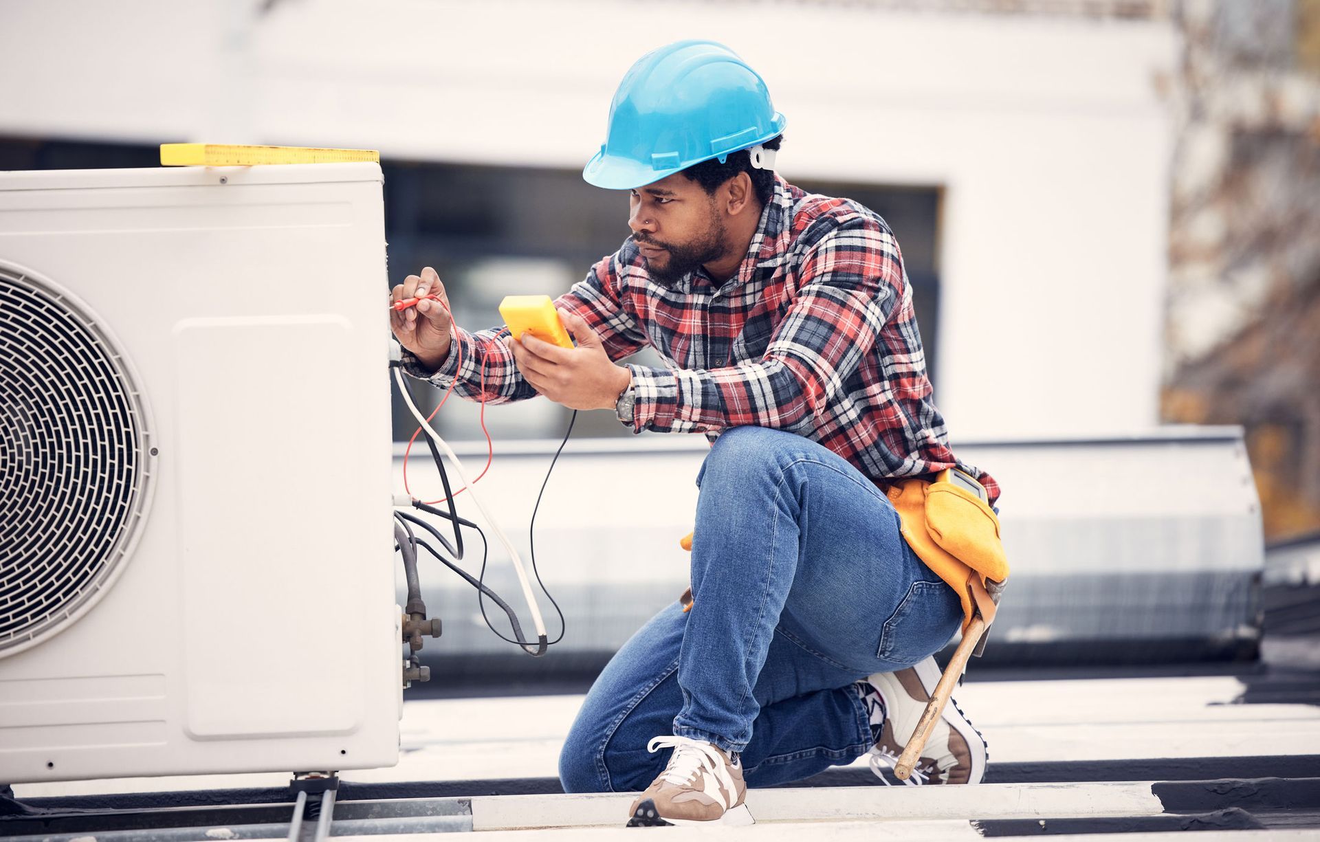 A man wearing a hard hat is kneeling down and working on an air conditioner.