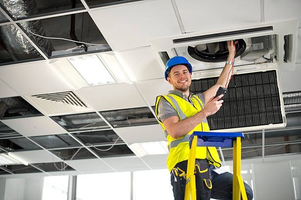 A man is standing on a ladder working on an air conditioner.