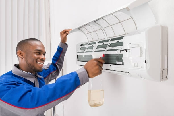 A man in a blue jacket is cleaning an air conditioner.