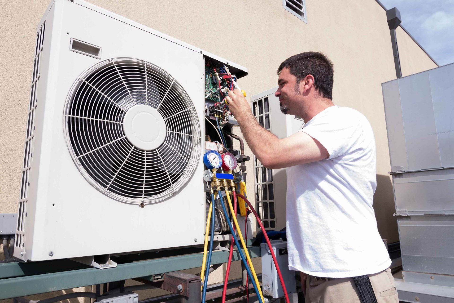 A man is working on an air conditioner outside of a building.