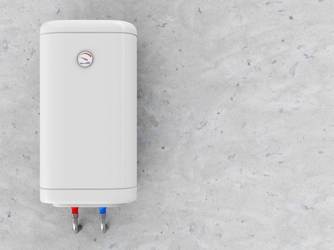 A white water heater is hanging on a concrete wall.