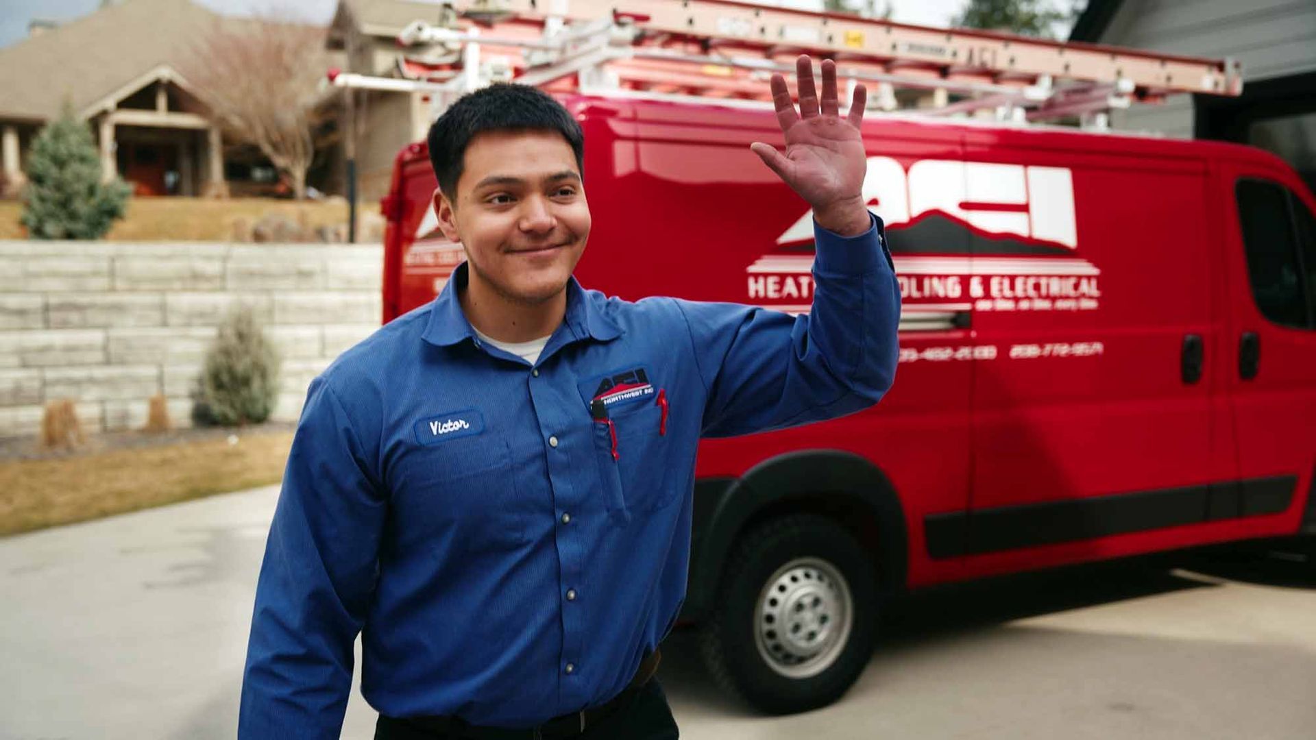 Smiling HVAC technician in blue ACI Northwest shirt waving as he approaches customer's home