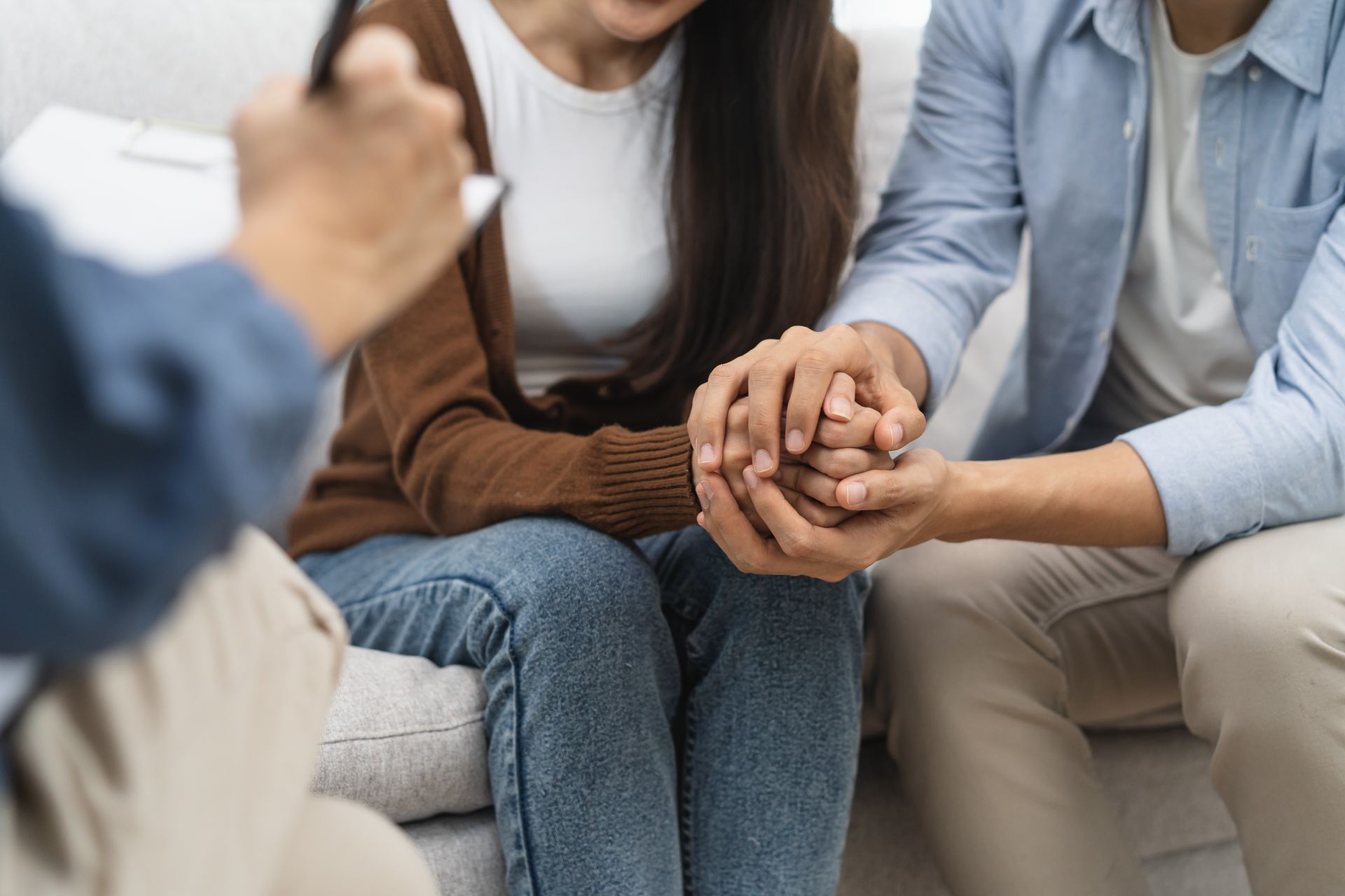 A man and a woman are holding hands while sitting on a couch.