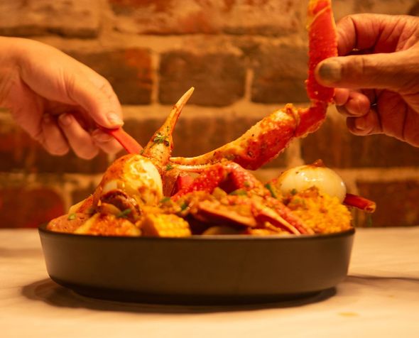 A person is holding a crab leg over a bowl of food.