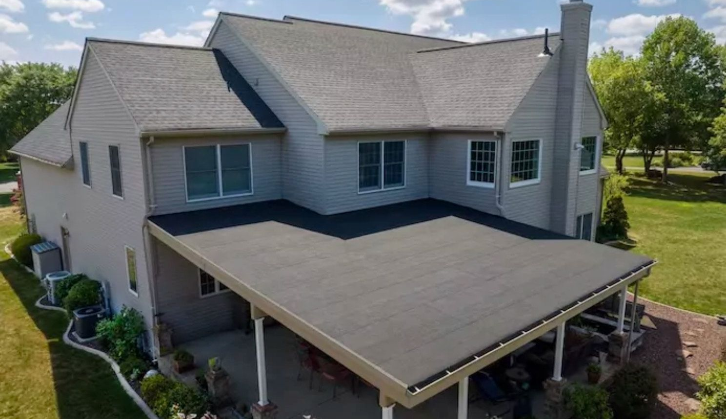 Two-story gray house with a black covered patio, set in a yard with trees.