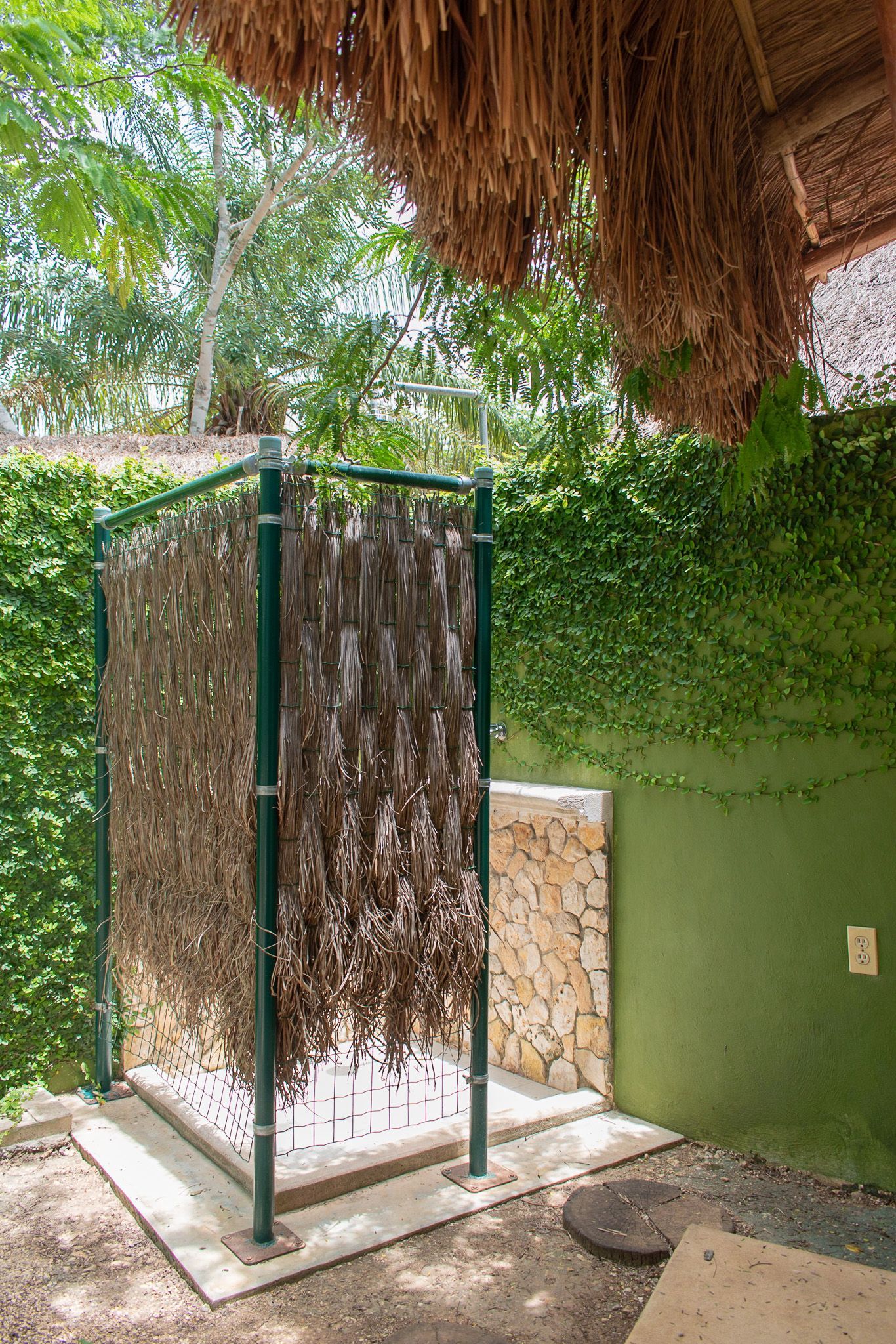 Una ducha al aire libre con una pared verde y un techo de paja.