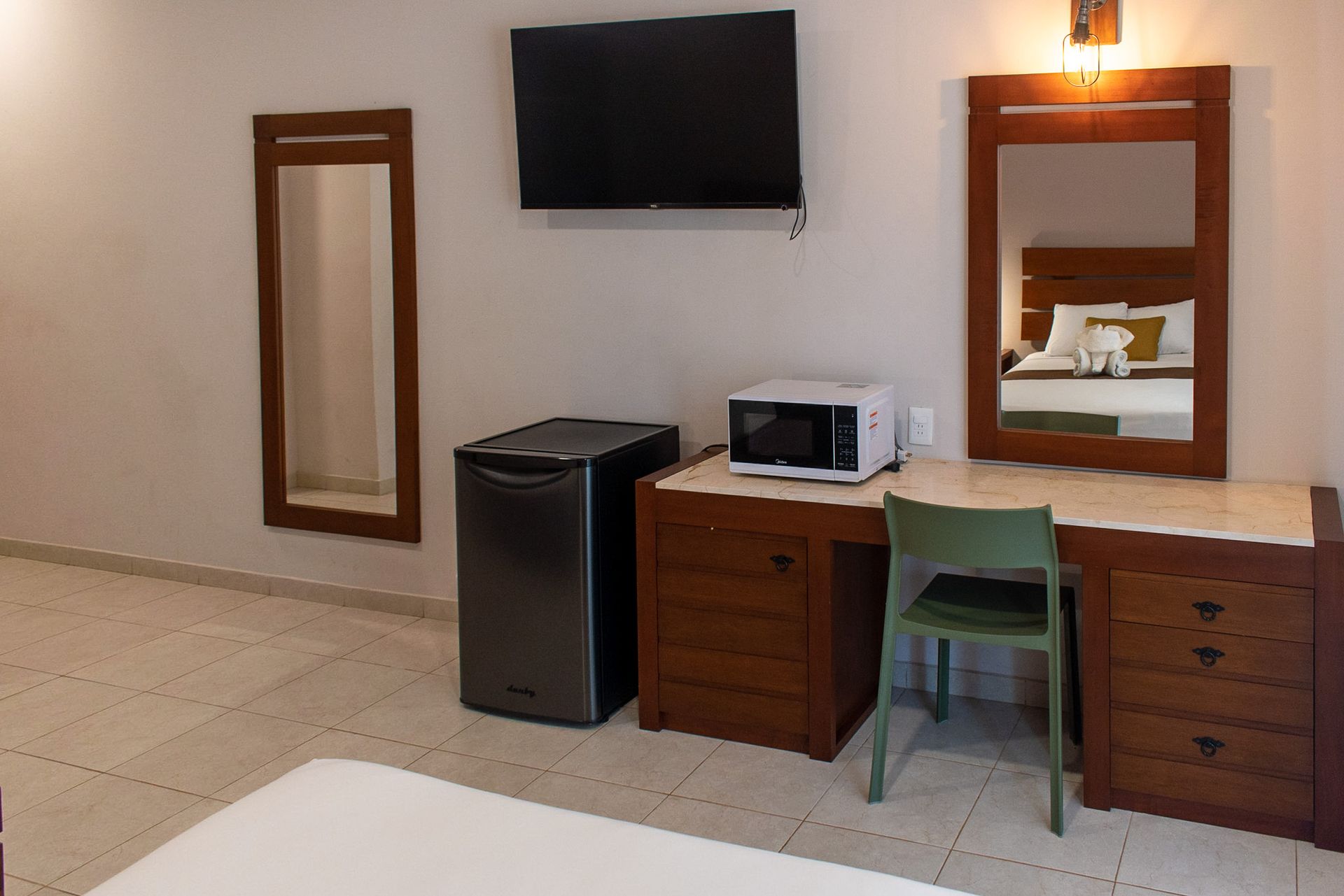 Una habitación de hotel con escritorio, silla, microondas, televisión y espejo.