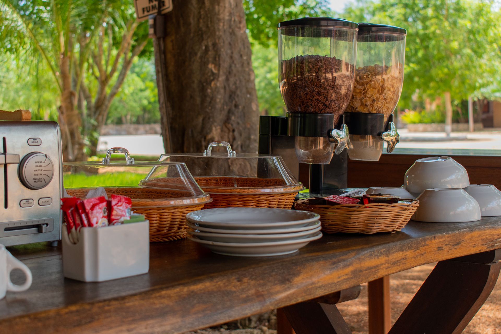 Una mesa de madera con platos, cuencos y una tostadora encima.