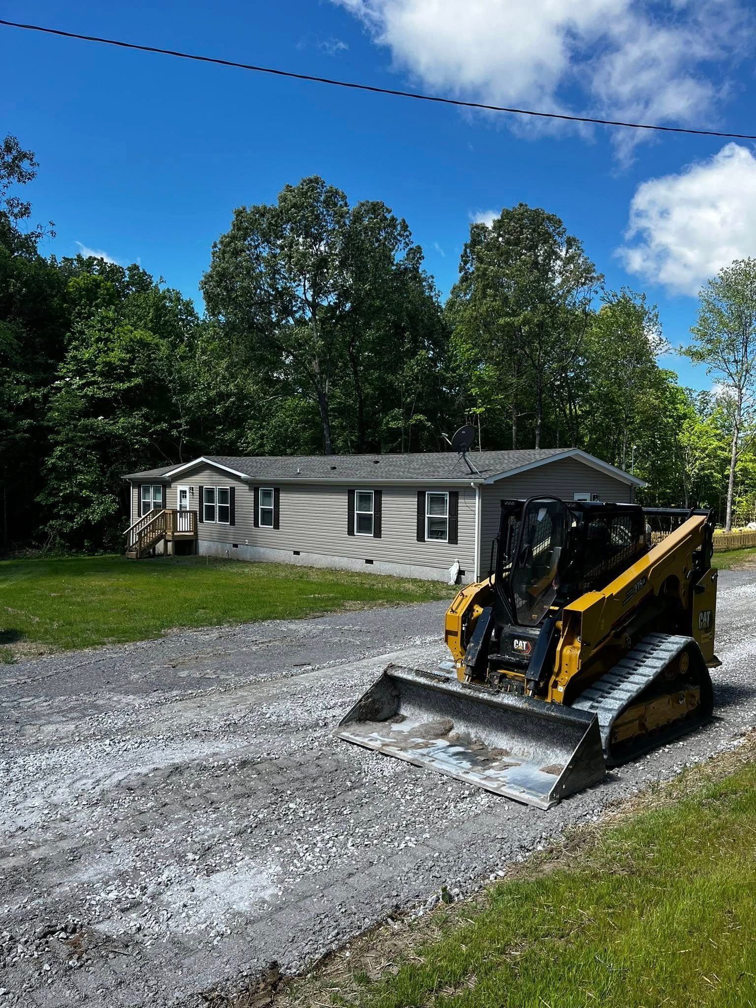 A bulldozer is driving down a gravel road in front of a mobile home.
