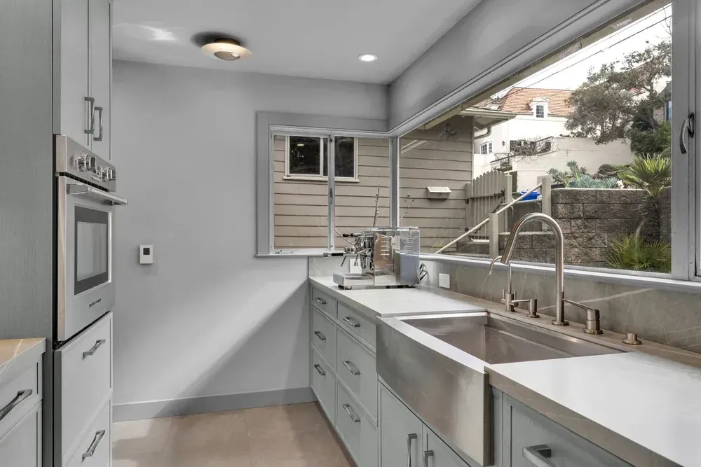 Modern kitchen with light blue cabinets, stainless steel sink, large window with outside view.
