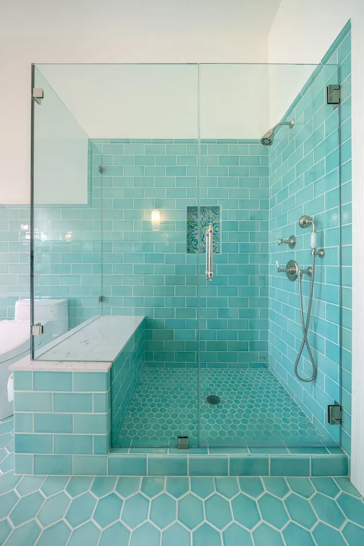 Aqua-tiled shower with glass doors, built-in bench, and pebble floor. Modern bathroom design.