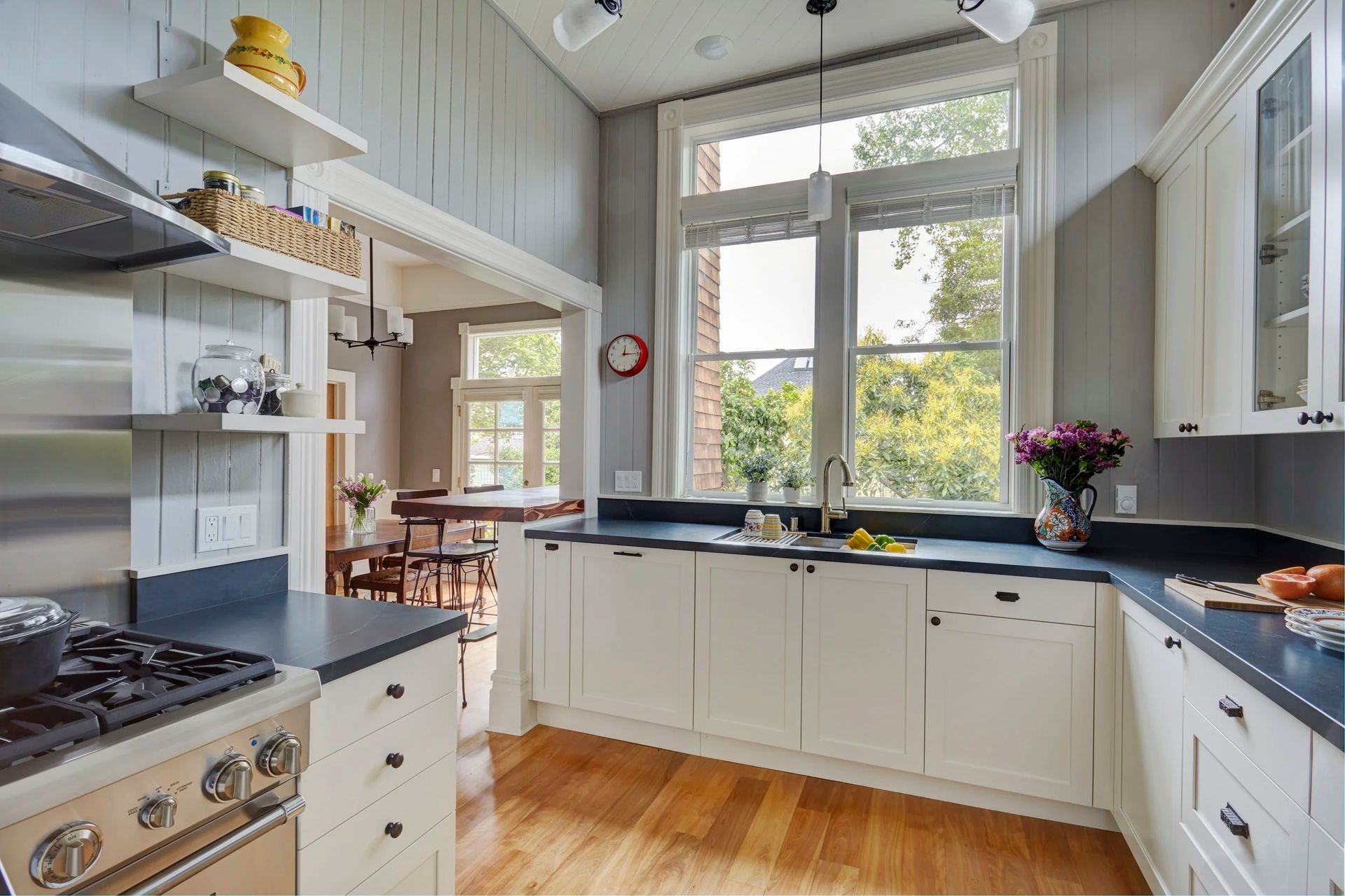 Kitchen with white cabinets, blue countertops, and a large window overlooking trees.