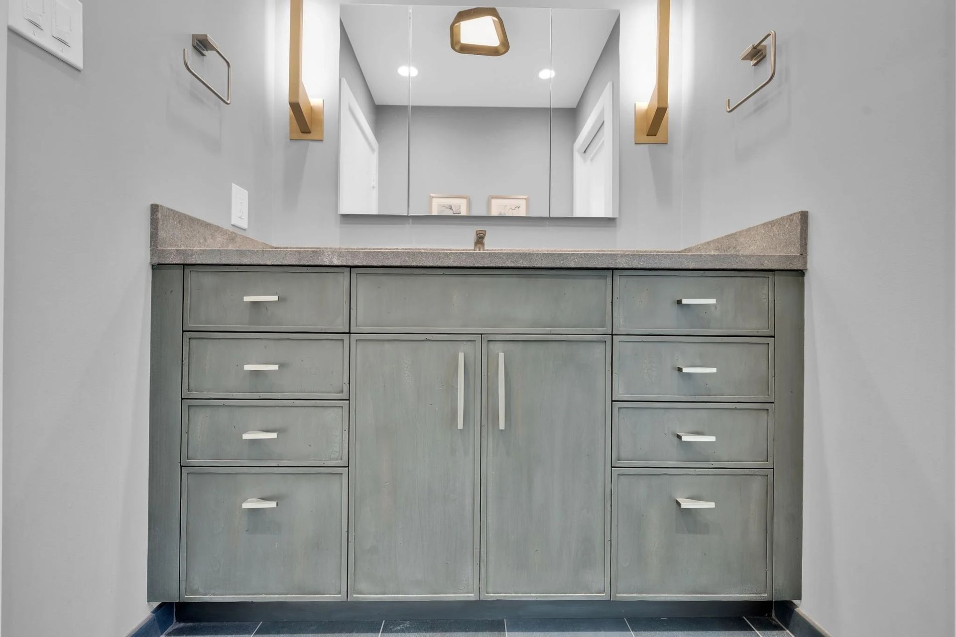 Gray bathroom vanity with drawers and cabinets, granite countertop, mirror, and sconces.