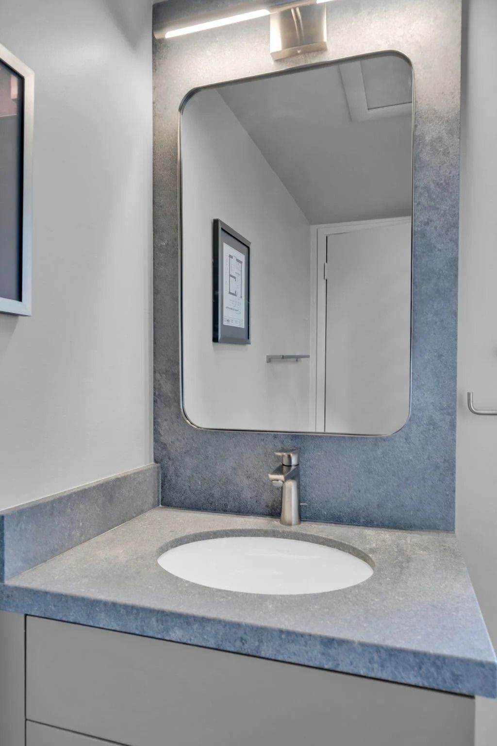 Bathroom with gray countertop, oval sink, and framed mirror with integrated light.