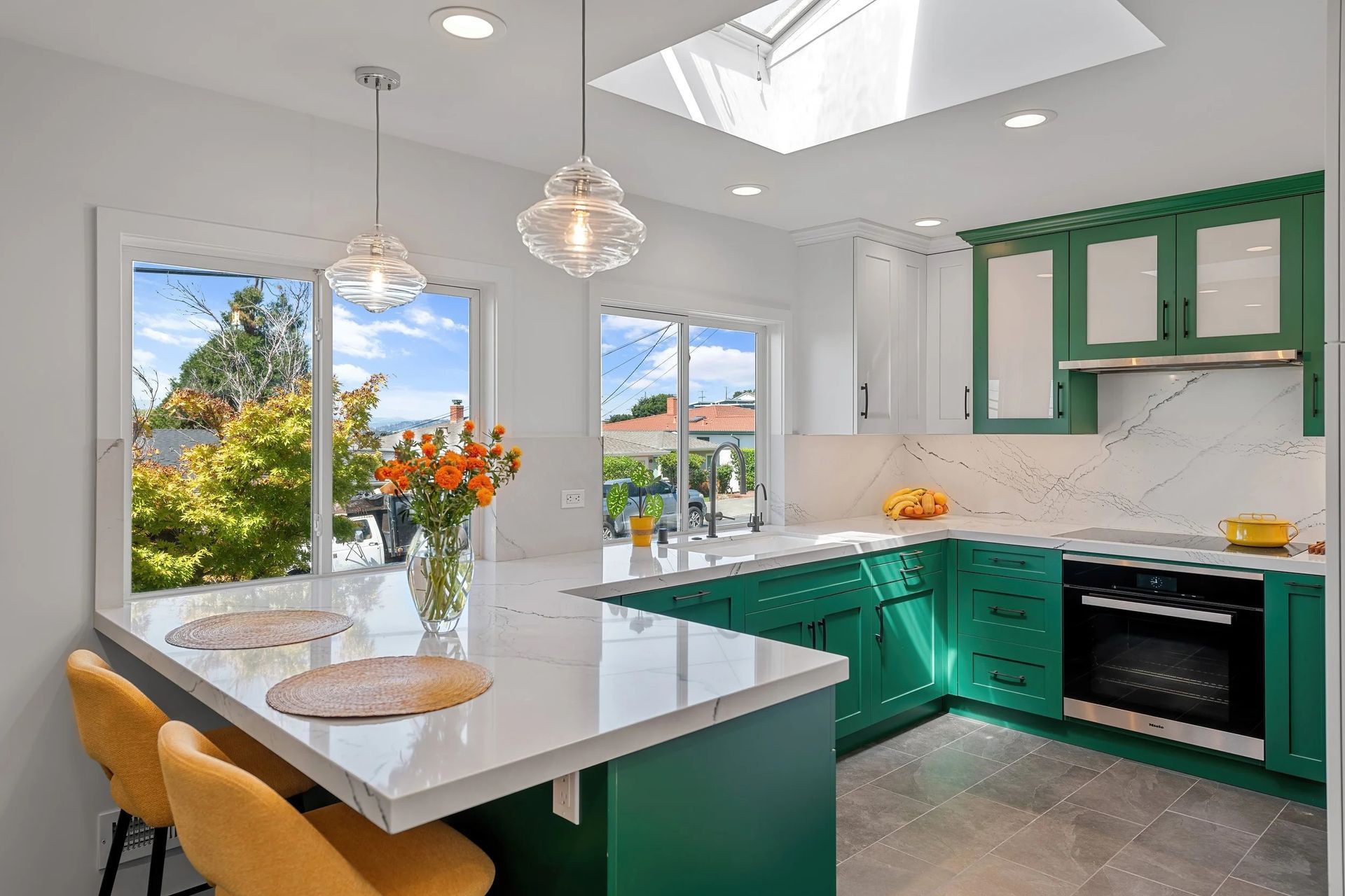 Modern kitchen with green cabinets, white countertops, and a skylight.