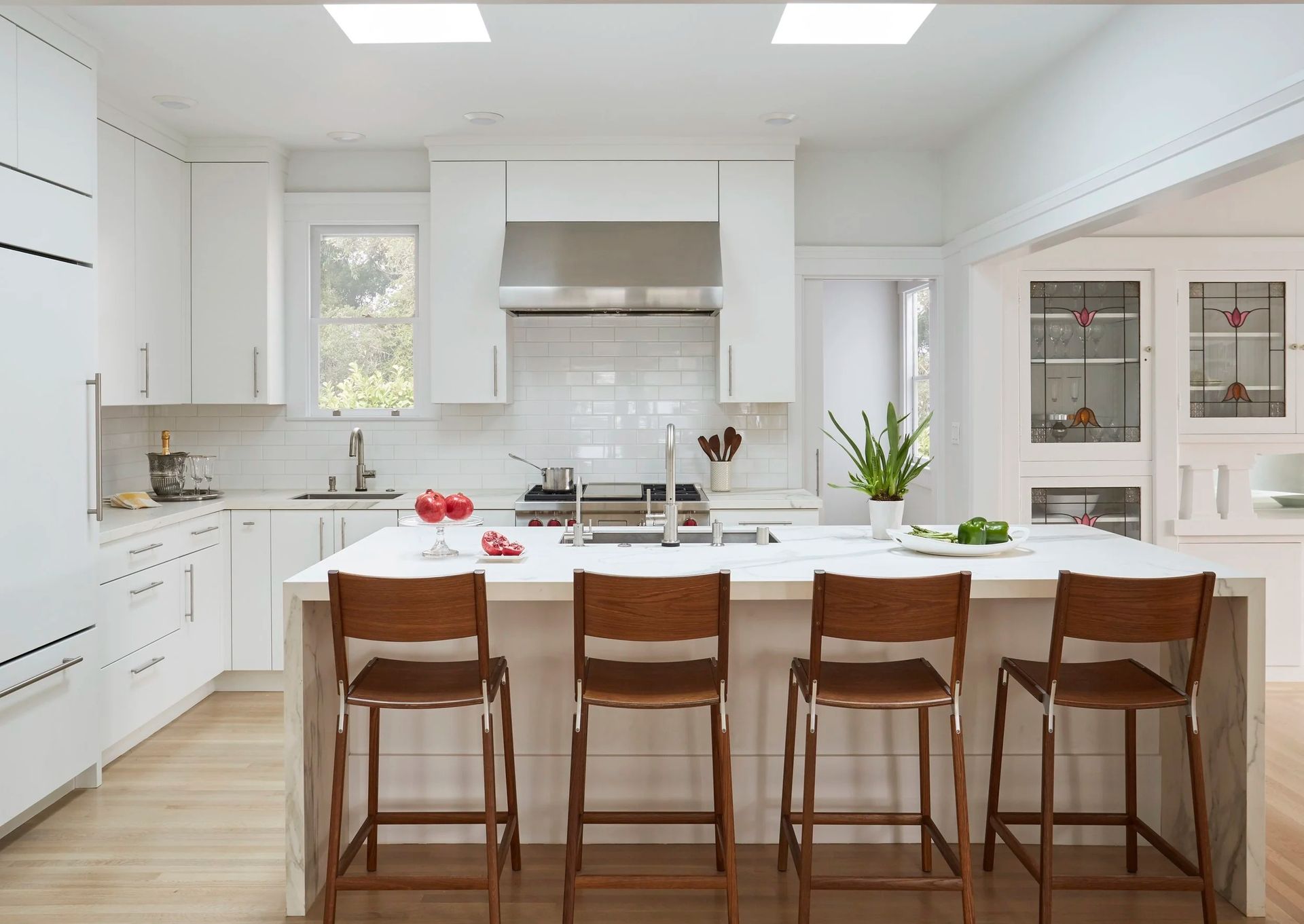 White kitchen with island and wooden bar stools. Two skylights provide natural light.