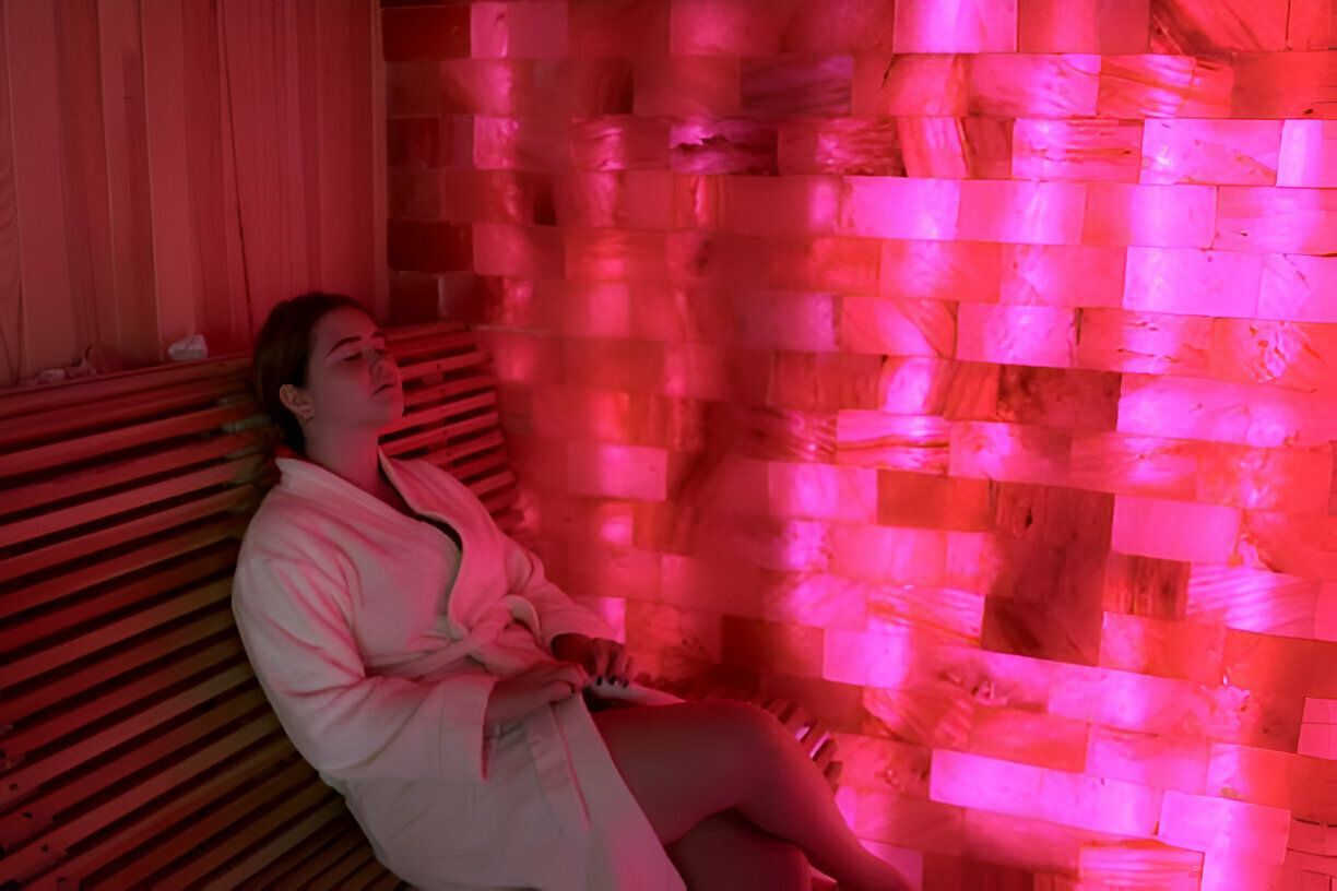 A woman is sitting on a bench in a salt room with pink lights.