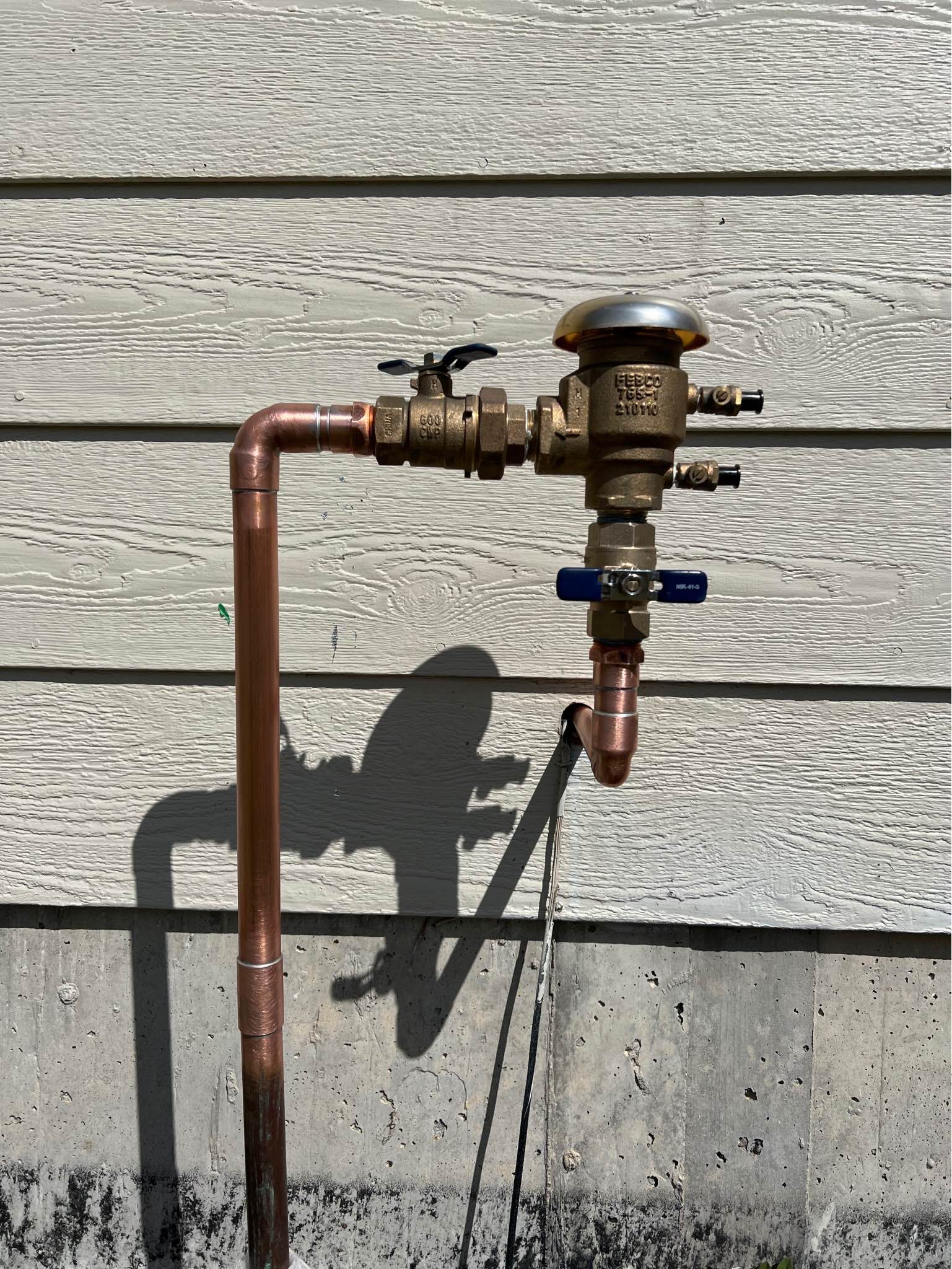 A copper pipe is attached to a faucet on the side of a building.