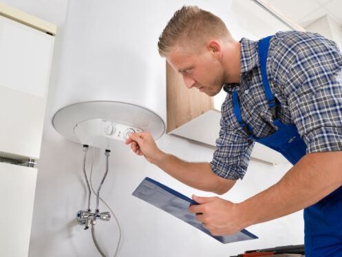 A man is looking at a water heater while holding a clipboard.