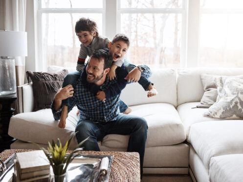 A man is sitting on a couch with two children on his shoulders.