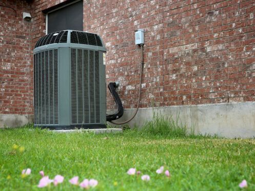 An air conditioner is sitting in the grass in front of a brick building.