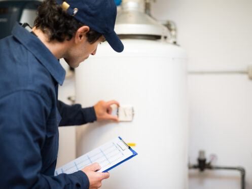 A man is looking at a water heater while holding a clipboard.