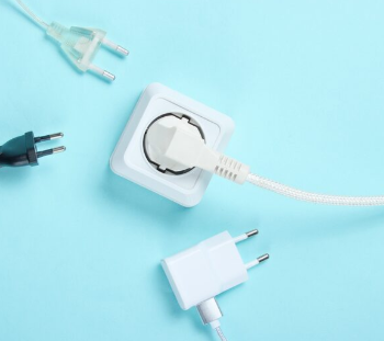 Tomacorriente eléctrico de color blanco con un enchufe insertado, rodeado de otros tres enchufes sobre una superficie azul.