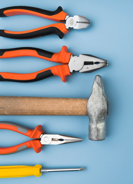 Herramientas manuales, incluidos alicates, un martillo y un destornillador, colocadas sobre una superficie azul.