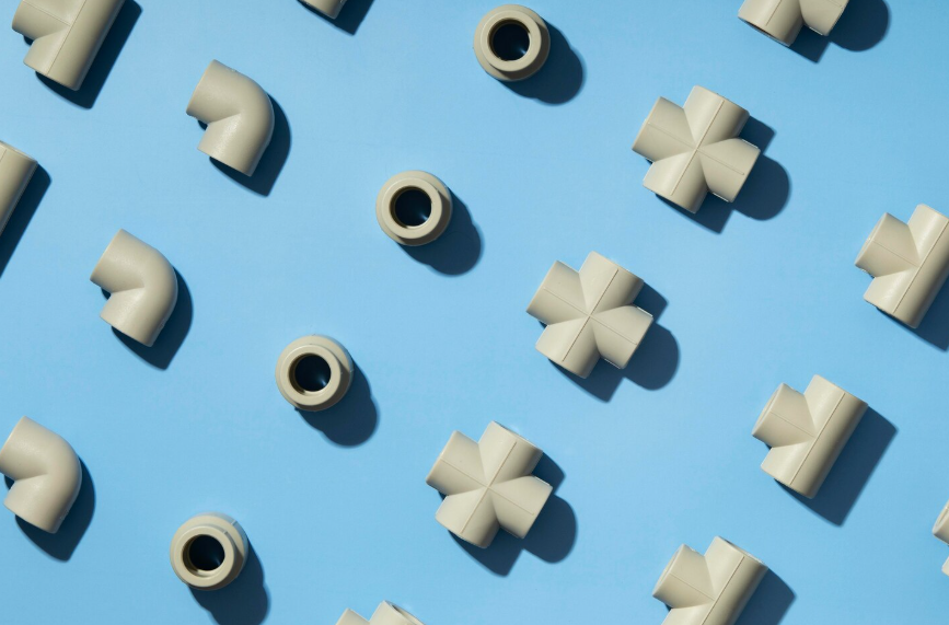 Accesorios de plomería de colores claros dispuestos en diagonal sobre un fondo azul: codos, tes y acopladores.