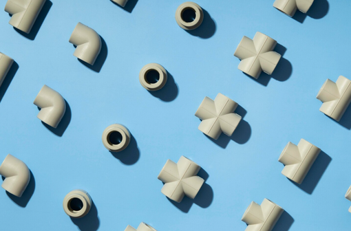 Accesorios de plomería de colores claros dispuestos en diagonal sobre un fondo azul: codos, tes y acopladores.