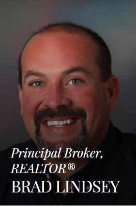 Brad Lindsey, Principal Broker, Realtor. Smiling man with a goatee in front of a blurred background.