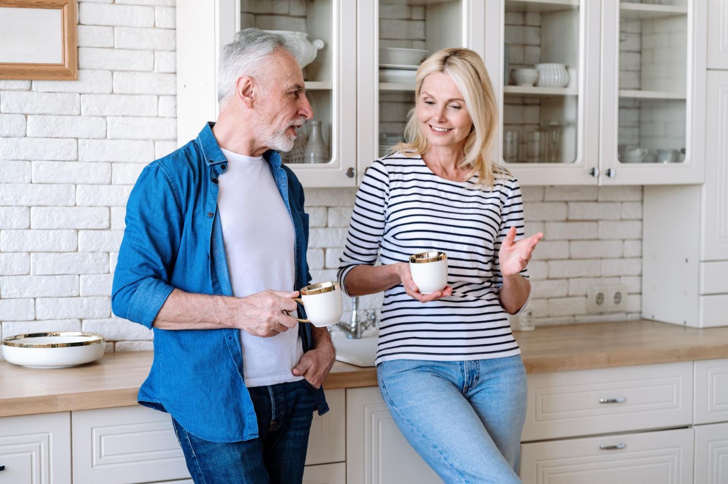 A man and a woman are standing in a kitchen holding cups of coffee.