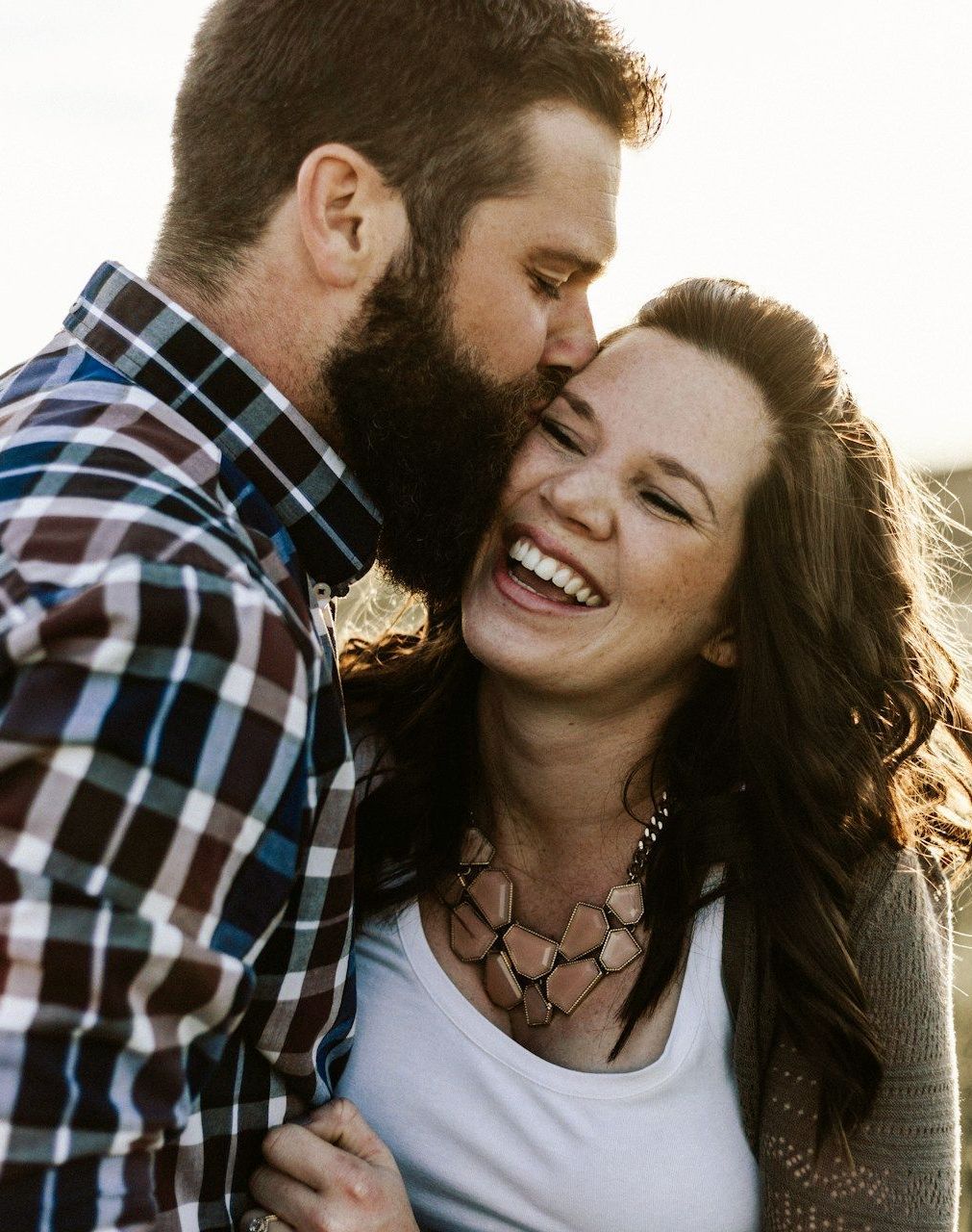 A man with a beard is kissing a woman on the cheek.