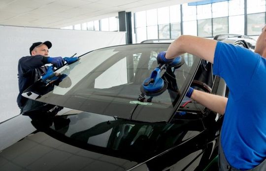 workers replacing windshield on black car