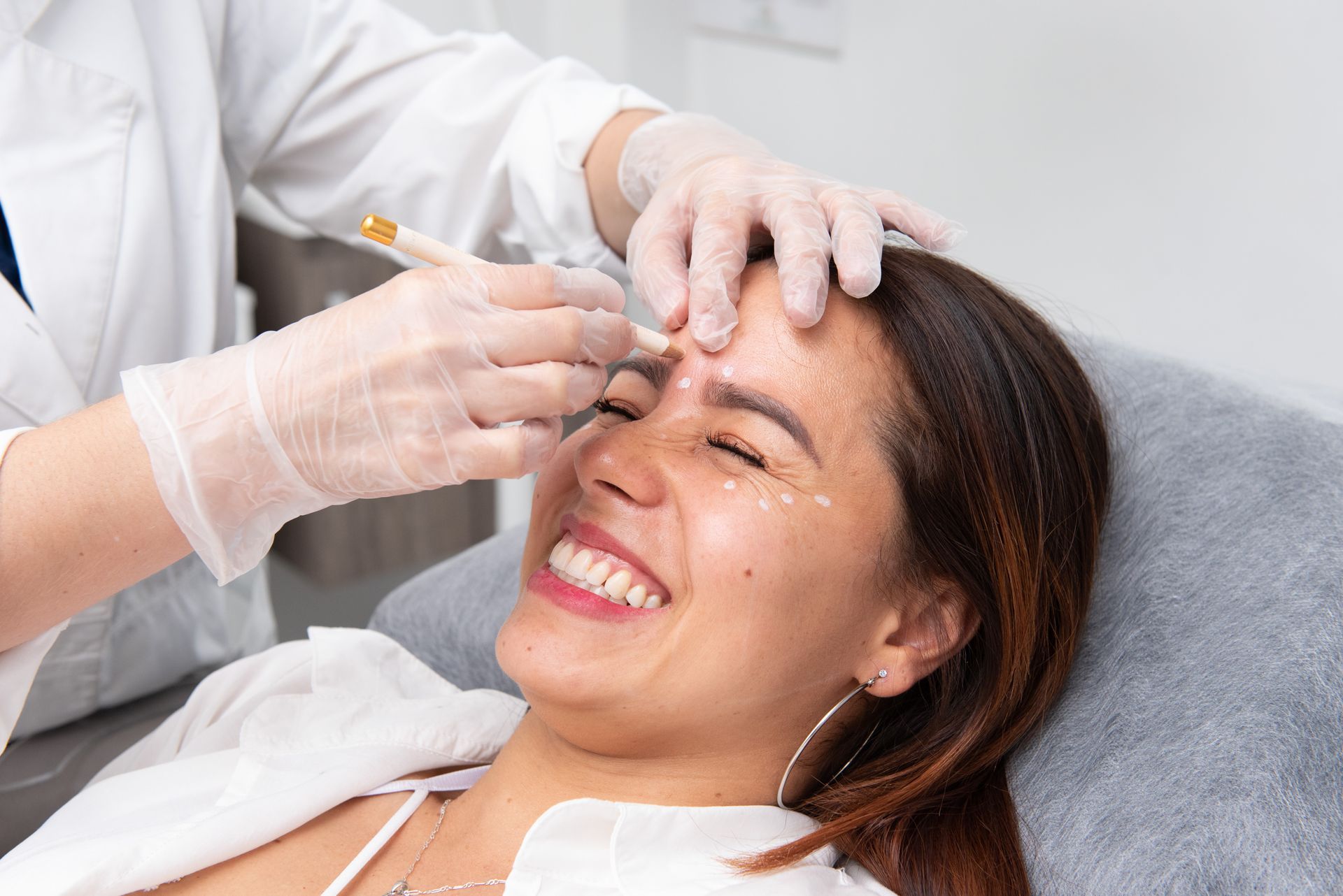 Una mujer sonríe mientras le ponen una inyección de botox en la frente.