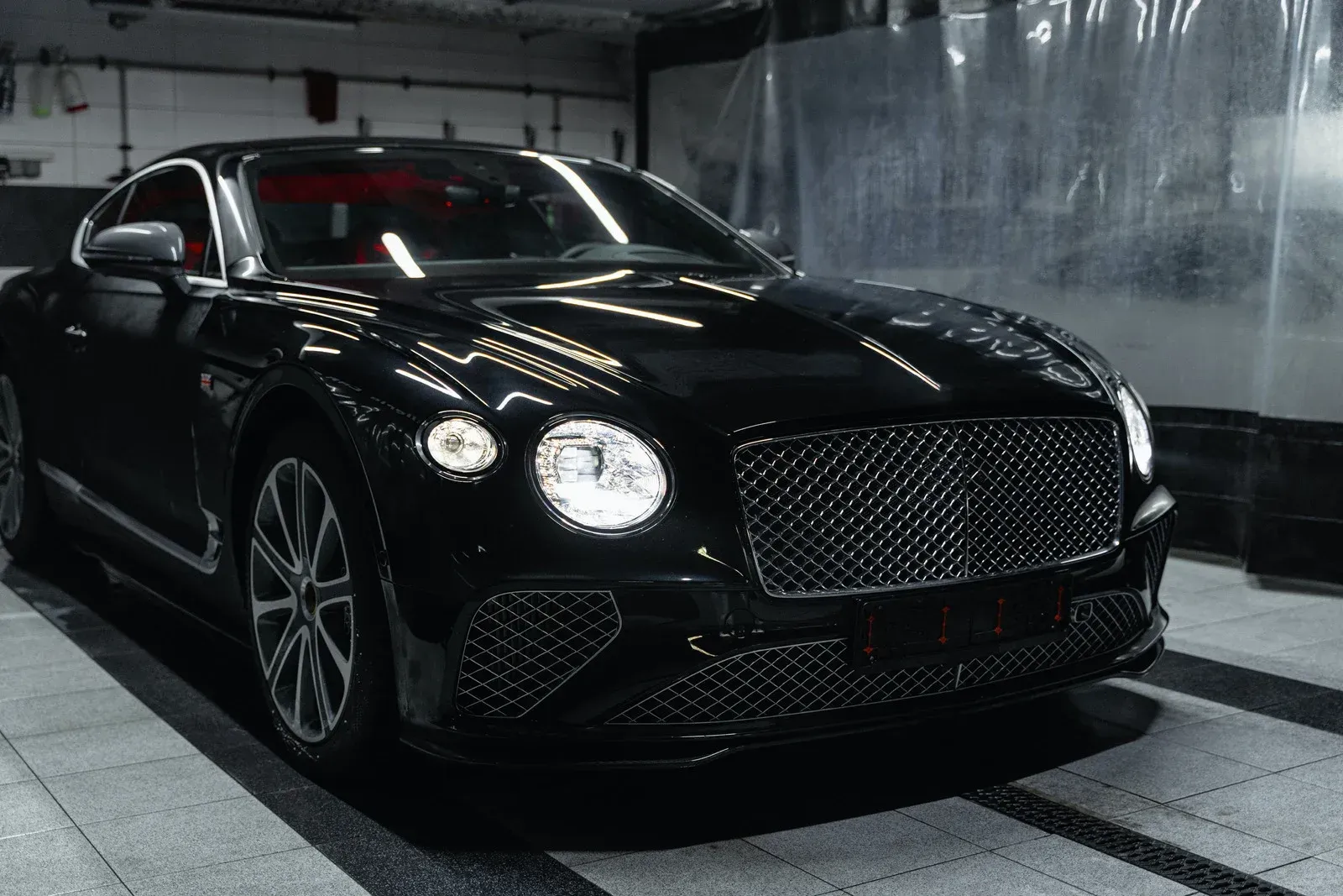 Black Bentley coupe car parked in a garage with bright lights, showcasing its details.