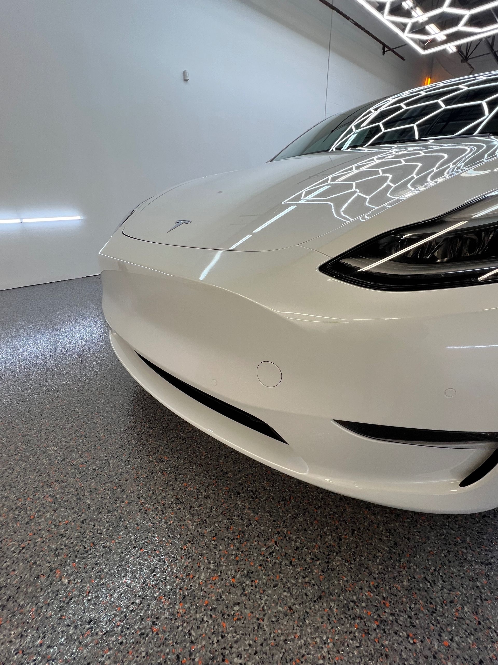 A white tesla model 3 is parked in a garage.