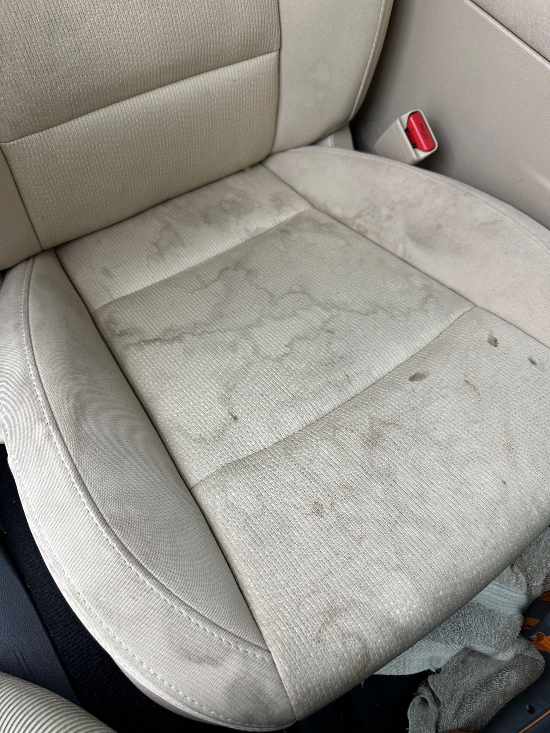 A dirty car seat with a red seat belt buckle