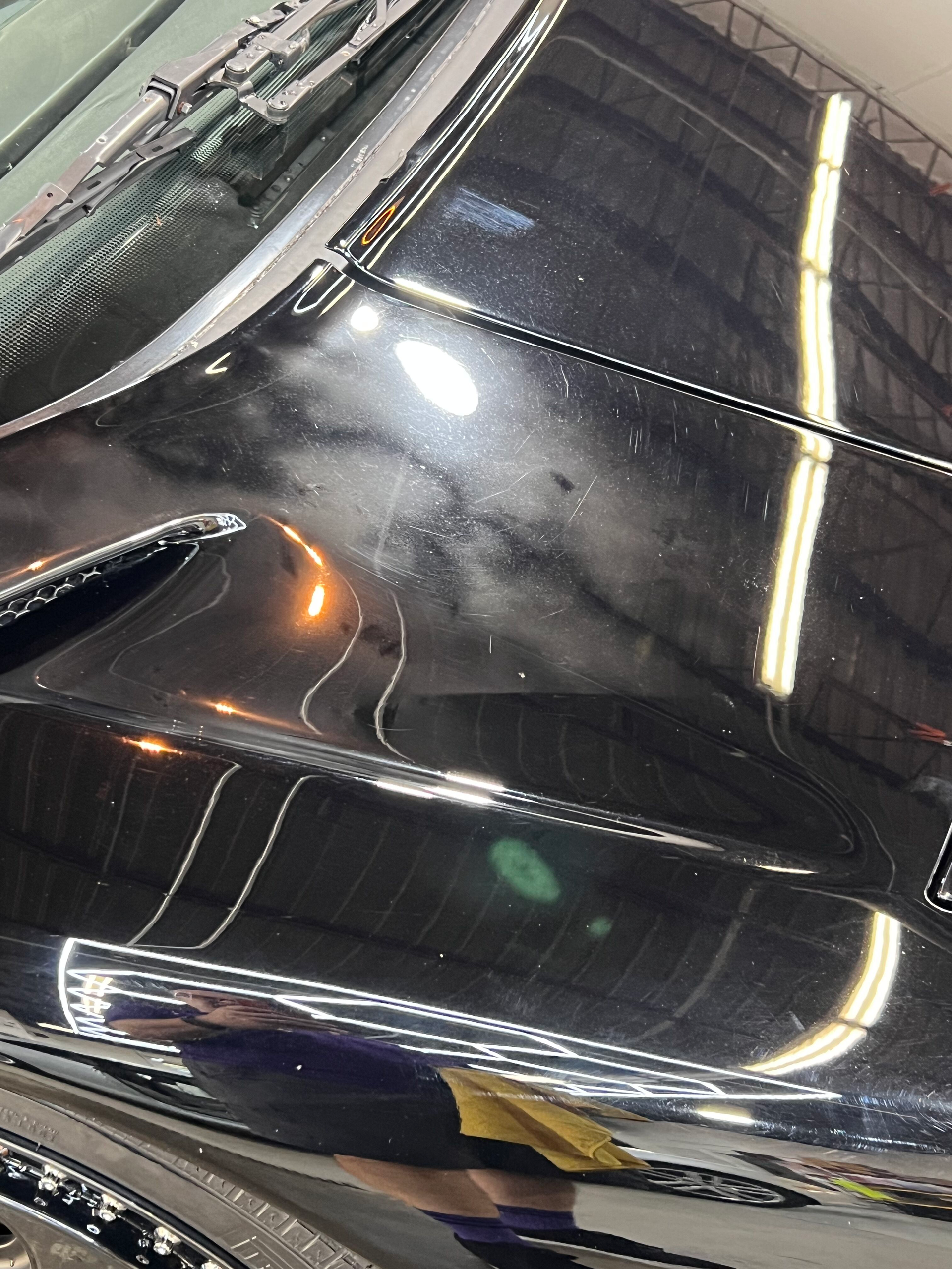 A close up of a black car 's hood in a garage.