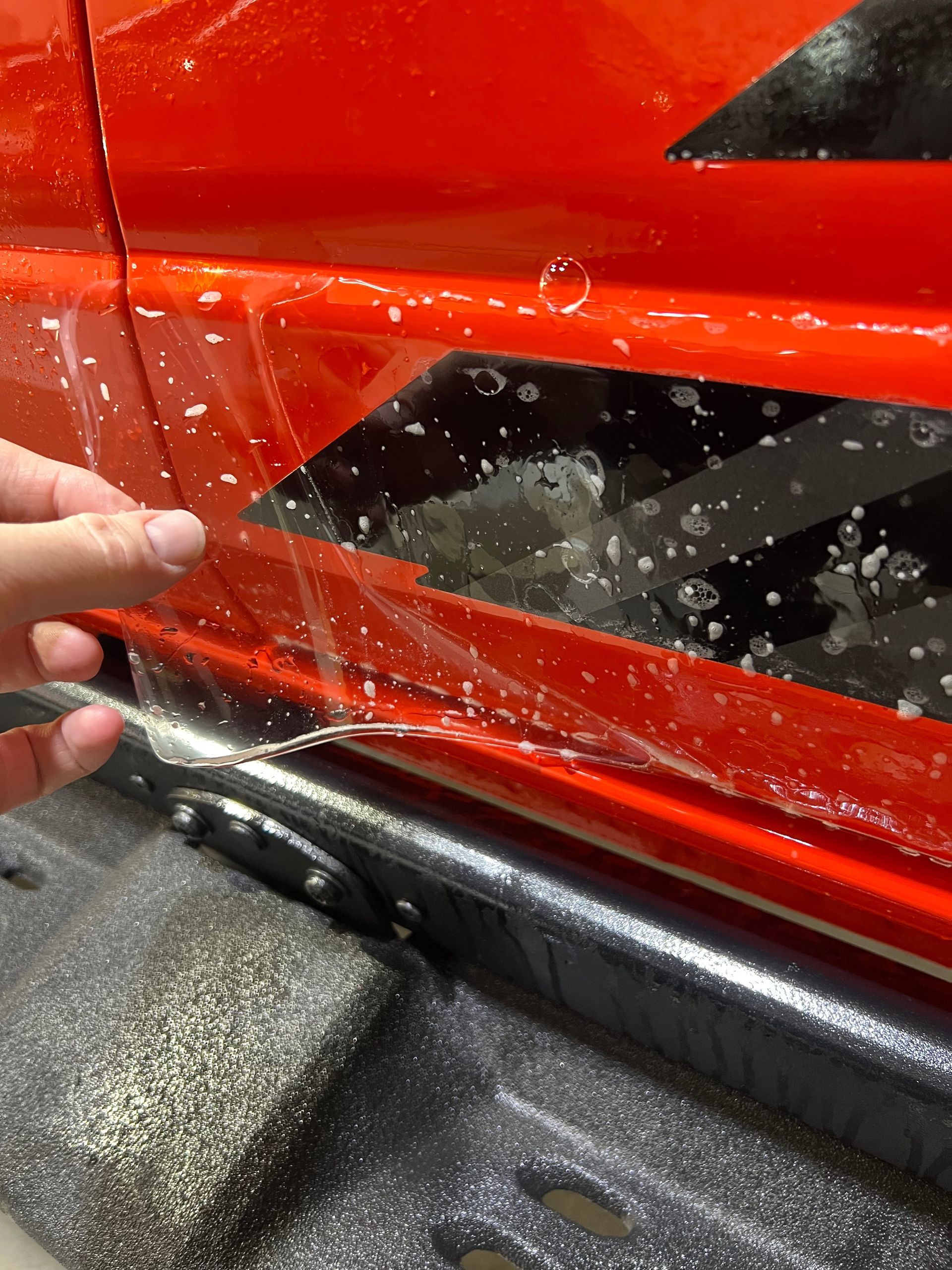 A person is holding a piece of plastic on a red car.