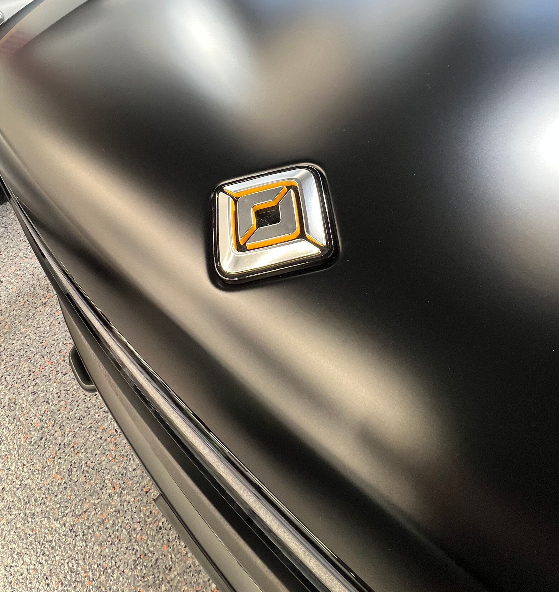 A close up of a black car with a square emblem on the hood