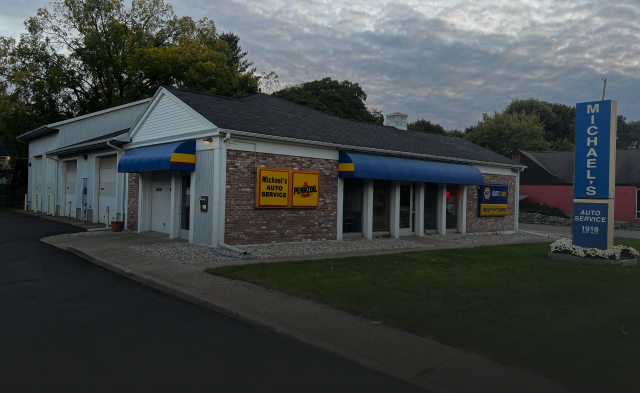 Michael's auto repair shop with blue awnings. White building with brick facade. Sign in front. | Michael's Auto Service