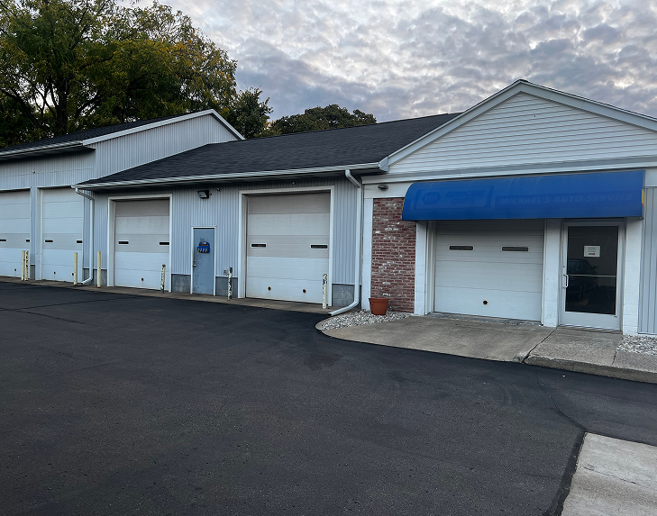 Exterior of a commercial building with multiple garage doors and a blue awning. Paved parking area in front. | Michael's Auto Service