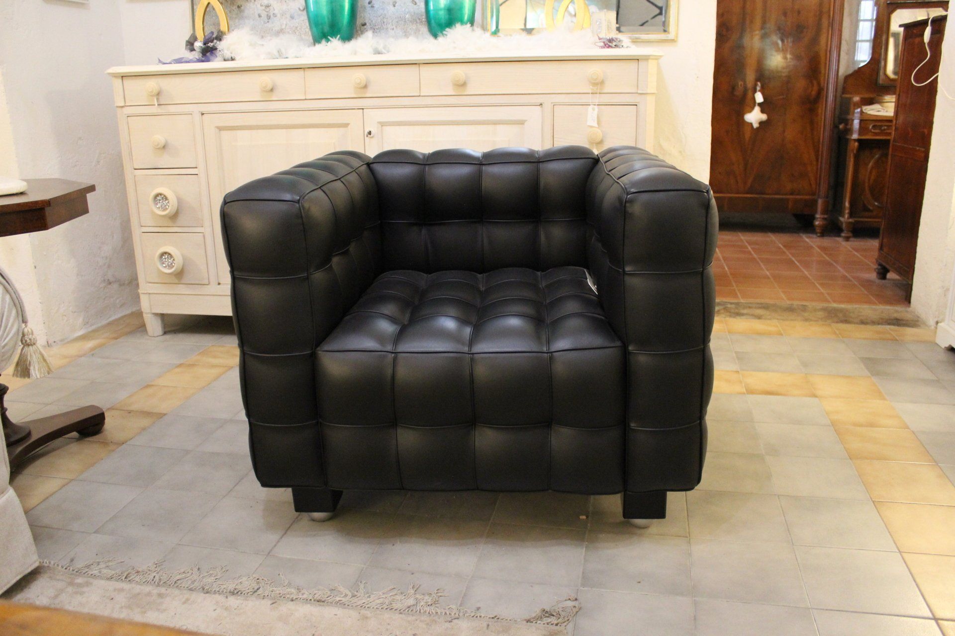 Poltrona cubica in pelle nera in una stanza con un mobile bianco e mobili in legno.