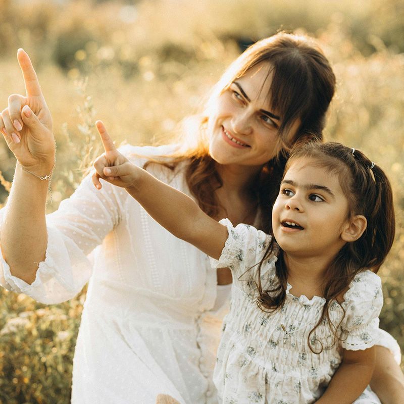Woman and child pointing upward in a sunlit flower field, smiling together