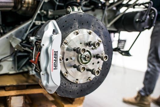 Ferrari brake assembly, silver caliper, drilled rotor, in workshop setting.